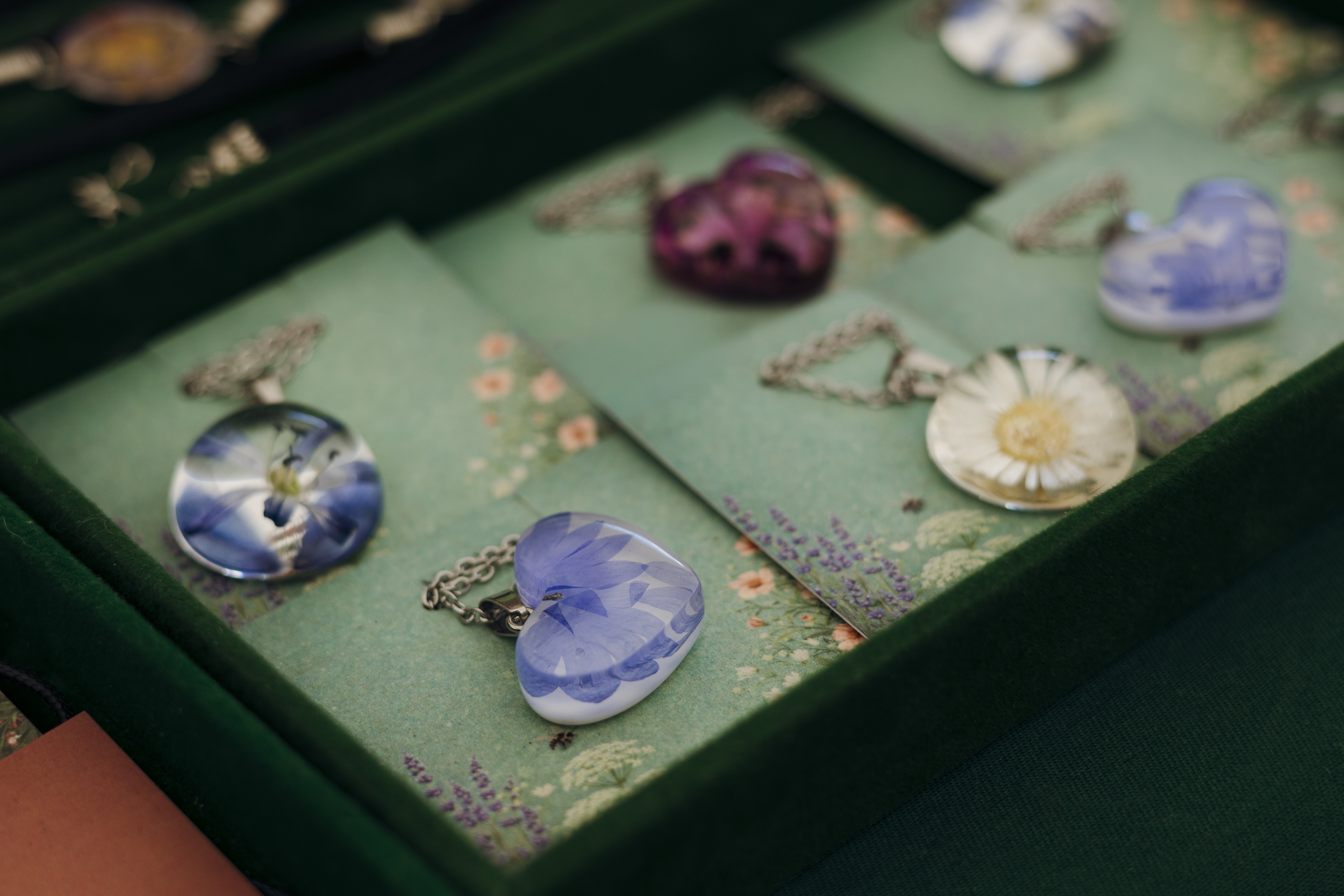 Collection of handmade resin pendants with real pressed flowers displayed at an artisan craft market. Botanical floral jewelry featuring unique handcrafted necklace designs.